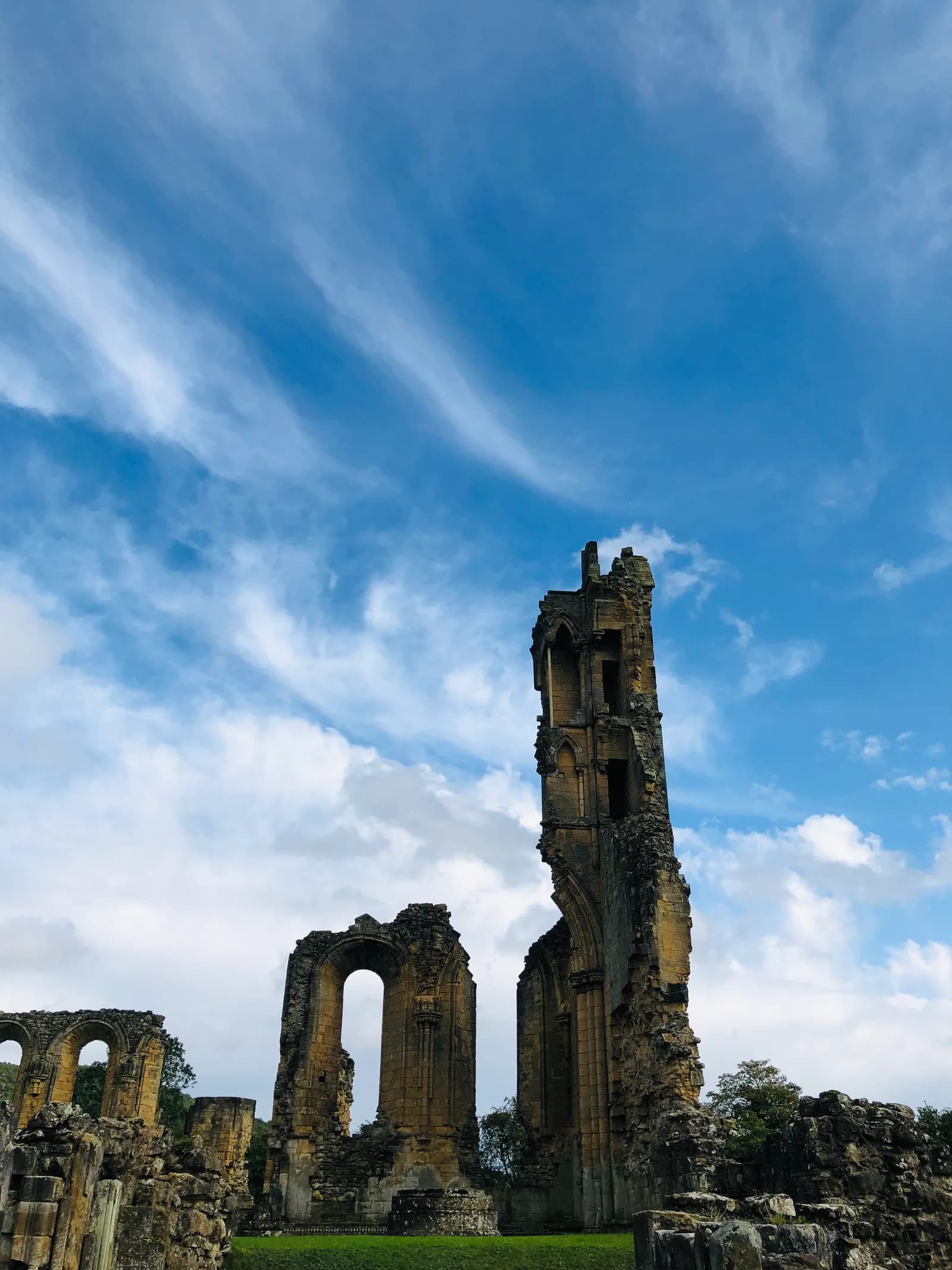 A towering stone archway in ruins under a bright blue sky with wispy white clouds.